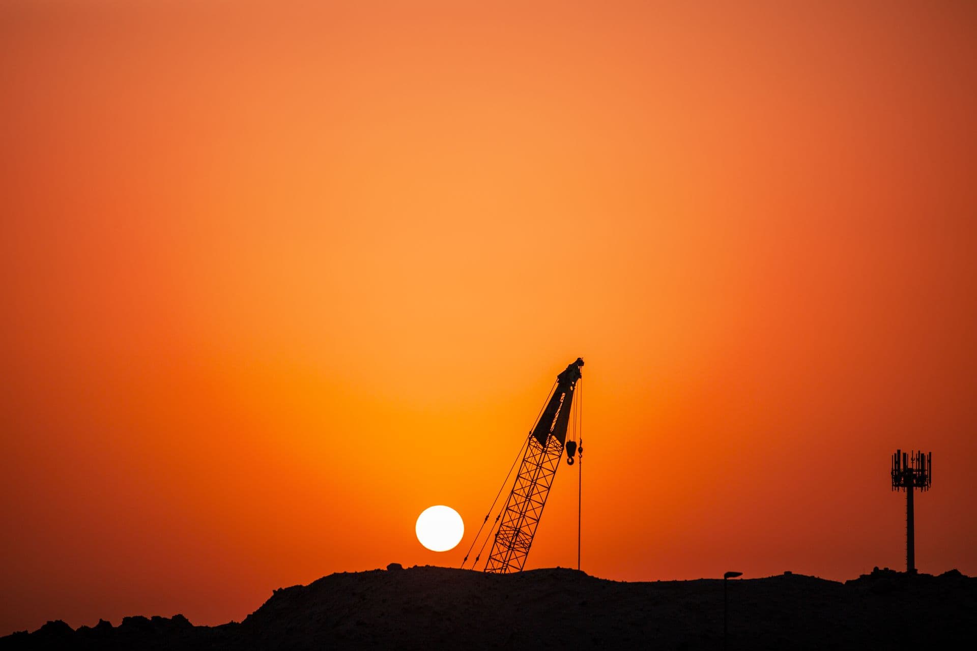 Construction crane silhouetted against a dramatic sunset sky