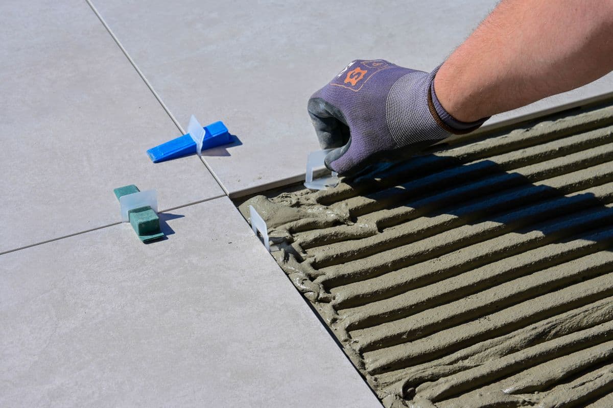 Detailed view of a gloved hand aligning floor tiles with levelers and spacers