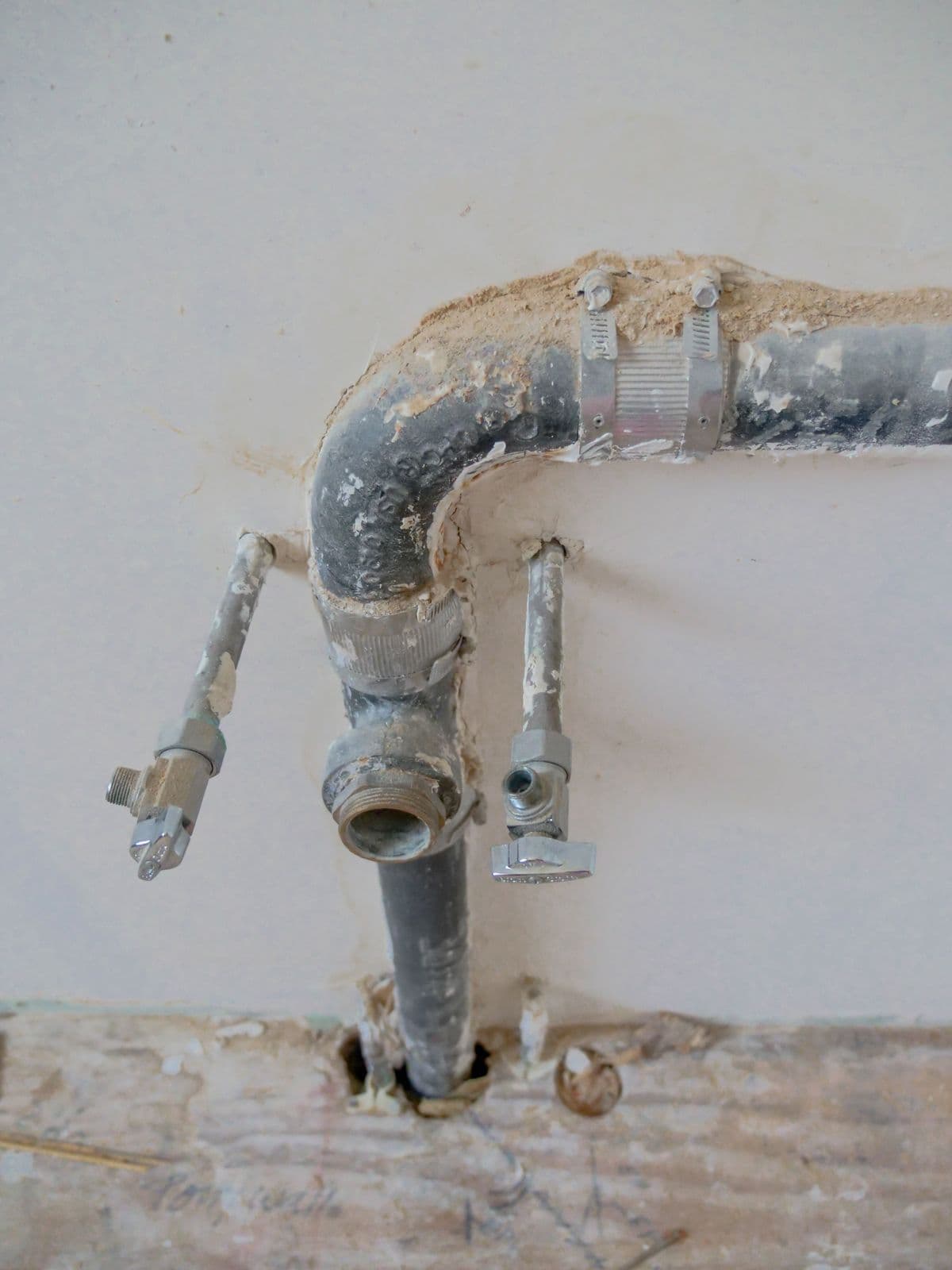 Close-up of exposed plumbing pipes on a construction site wall