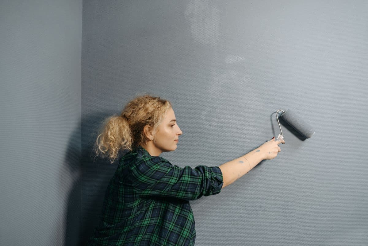 Young woman using a paint roller to apply grey paint on an indoor wall during renovation